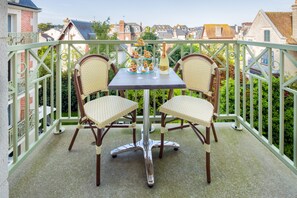 Ein Balkon mit zwei Korbstühlen und einem Tisch, gedeckt für eine Mahlzeit, mit Blick auf eine Wohngegend.