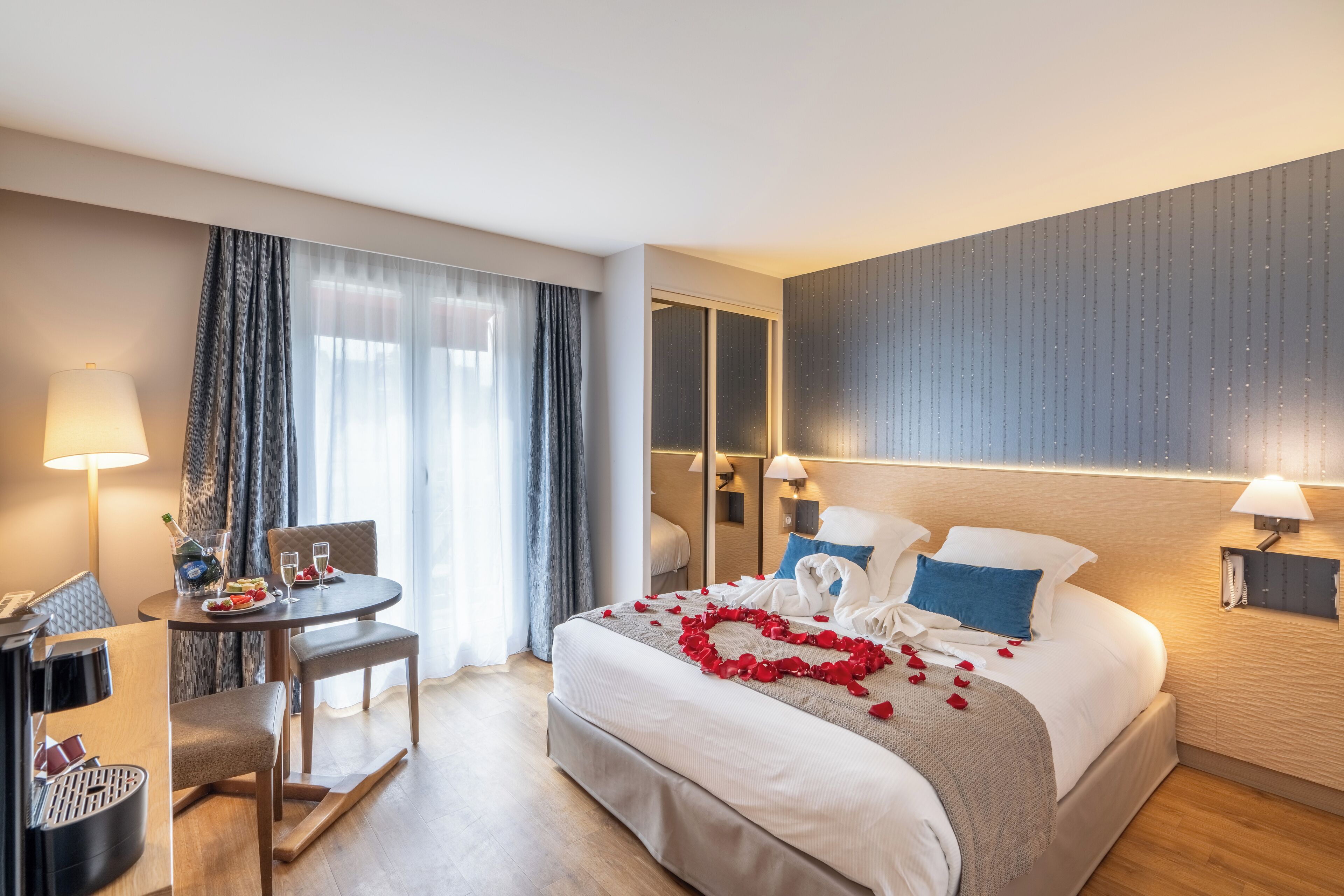 Una habitación de hotel con cama, escritorio, silla, lámpara y espejo.