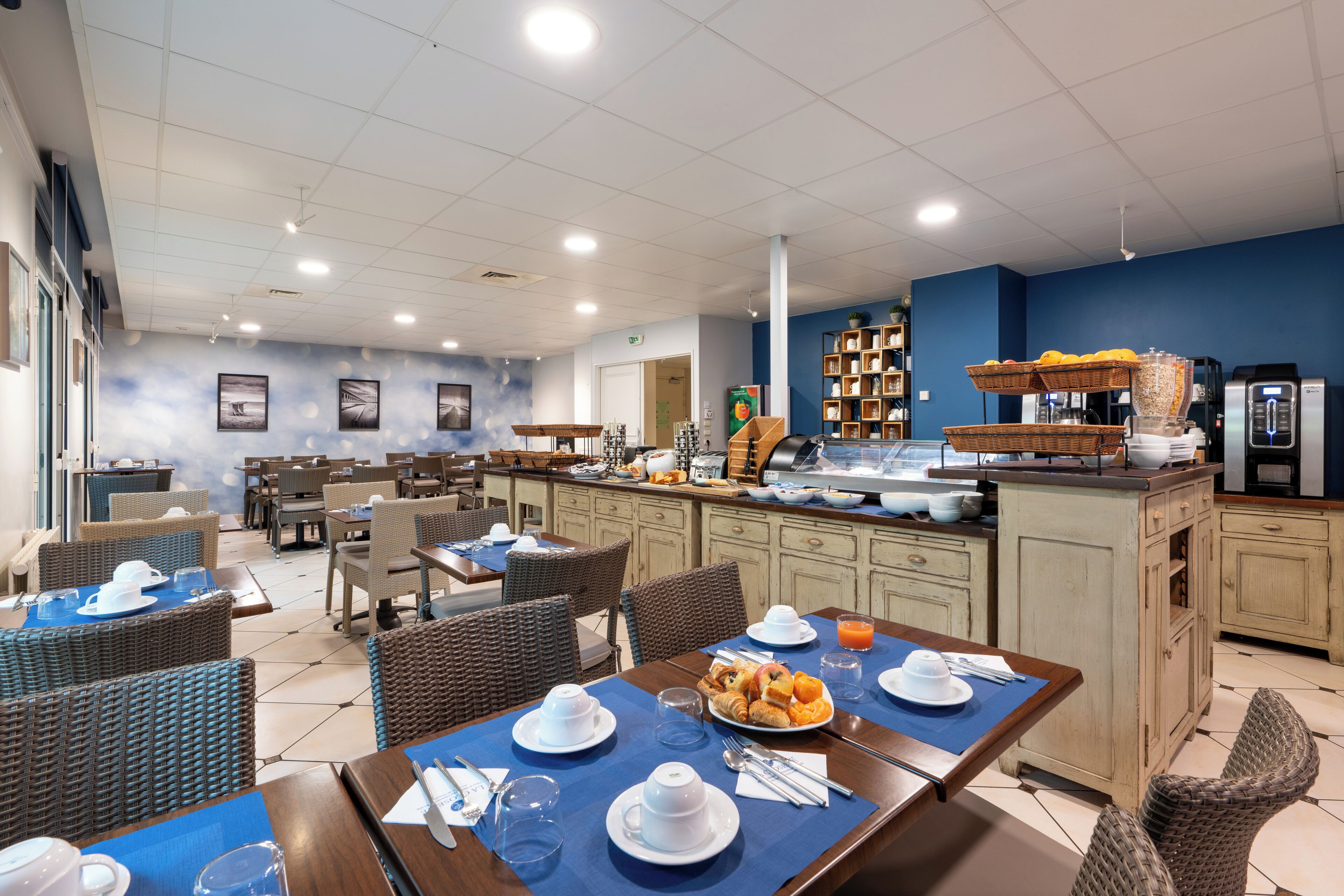 A breakfast area with tables set for dining, a buffet with various food items, and a kitchen area with appliances.