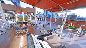 Une salle de sport équipée de divers appareils d’exercice, notamment des tapis de course et des appareils de musculation, située dans un espace abrité offrant une vue sur la ville.
