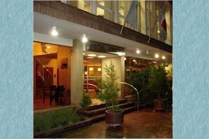 A hotel entrance with a glass facade, outdoor seating, and a small water feature.