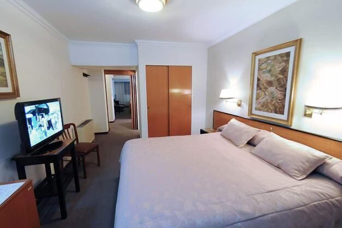 Una habitación de hotel con cama, escritorio con televisor, silla y puerta que da a otra habitación.
