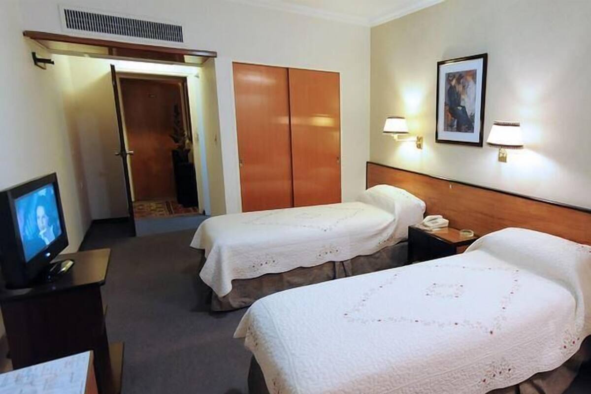 Habitación de hotel con dos camas, televisión, escritorio y puerta que da a un baño.