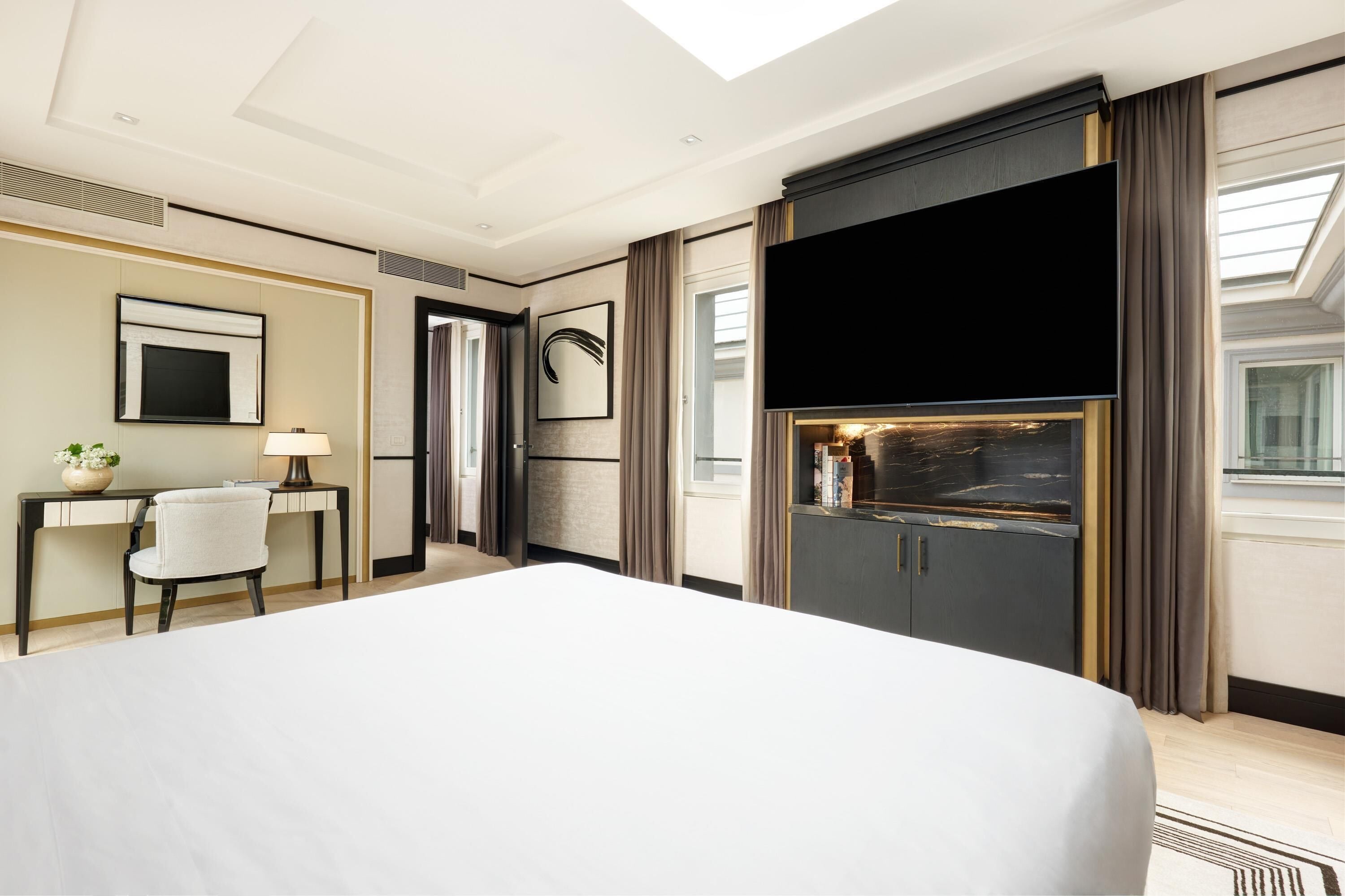 Ein Hotelzimmer mit einem großen Bett, einem Schreibtisch mit Stuhl, einem Flachbildfernseher und einer Minibar.