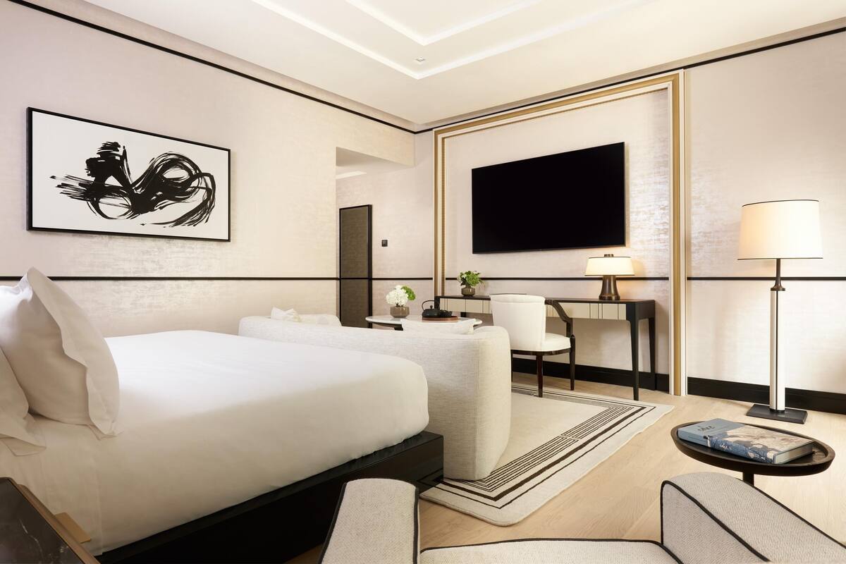 A modern hotel room with a large bed, a flat-screen TV, a desk with a lamp, and a painting on the wall.