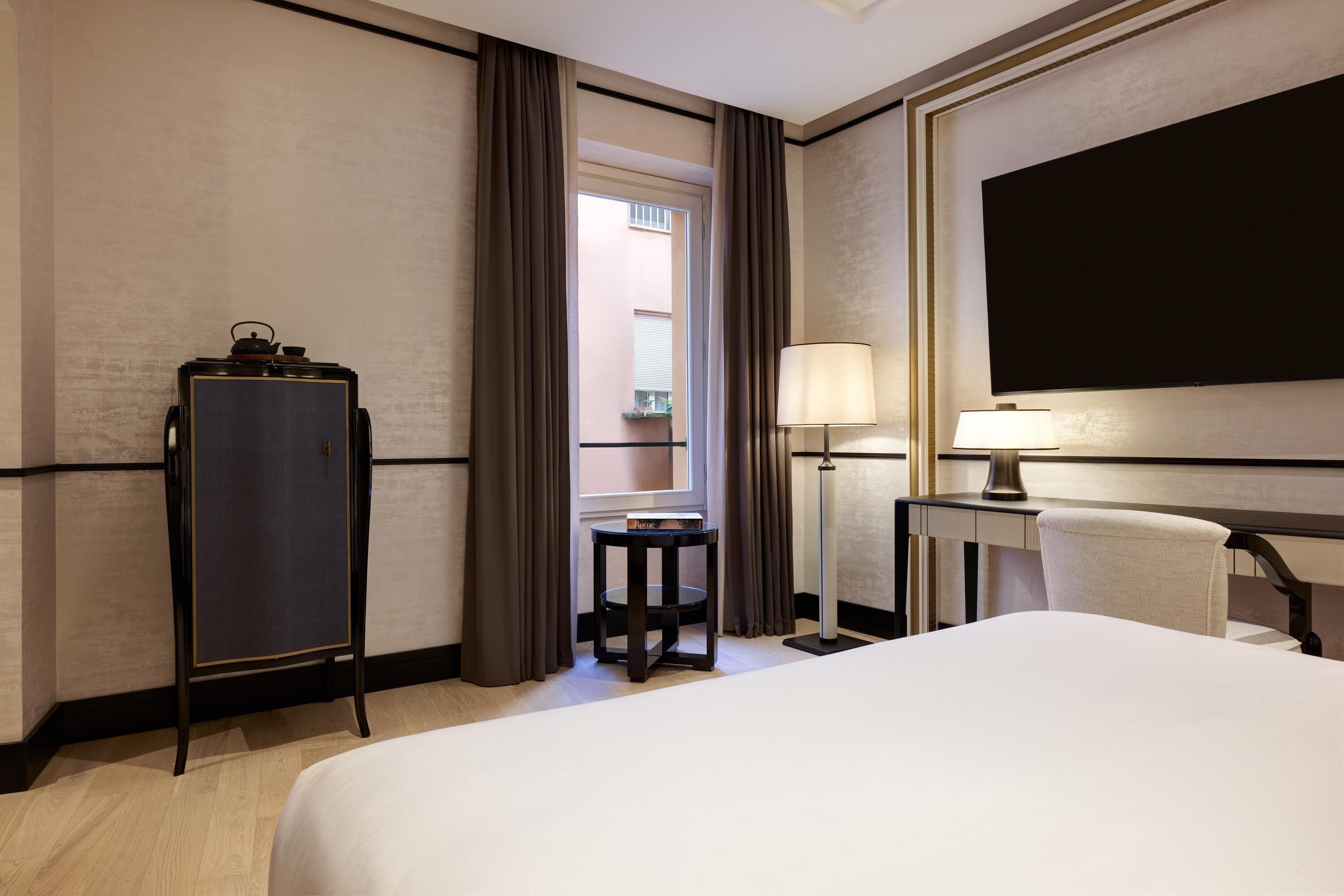 Una camera d'albergo con un letto, una scrivania con una lampada, una sedia, un armadio e vista all'esterno da una finestra.
