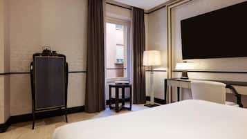 Una camera d'albergo con un letto, una scrivania con una lampada, una sedia, un armadio e vista all'esterno da una finestra.