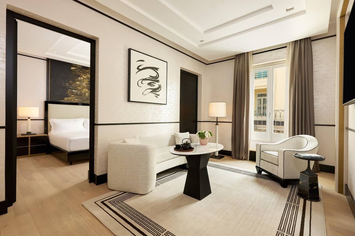 A modern hotel room with a bed, a sofa, a round table with a plant, and a TV.