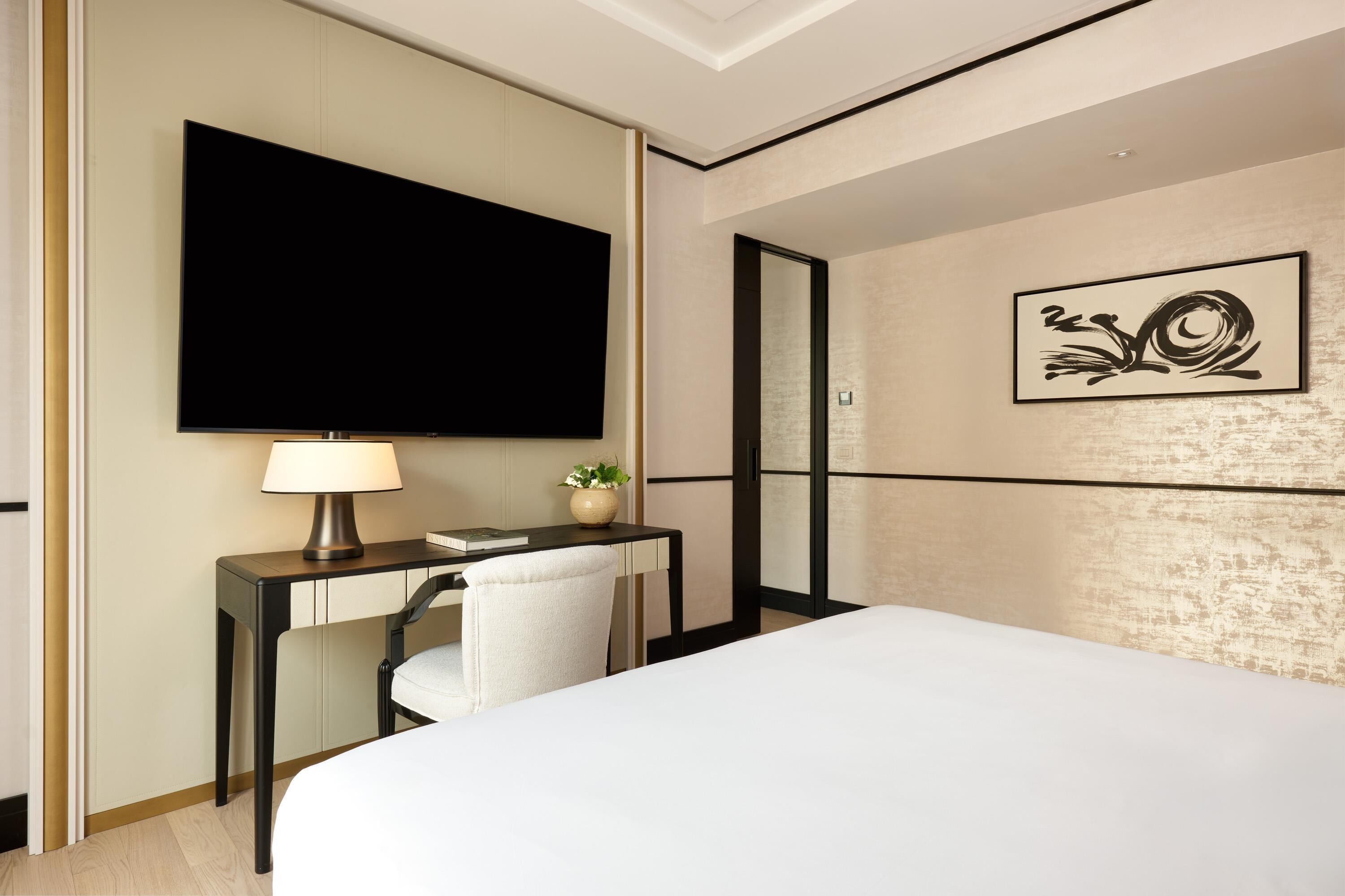 Una camera d'albergo con un letto, una scrivania con una lampada, una televisione e un quadro appeso al muro.