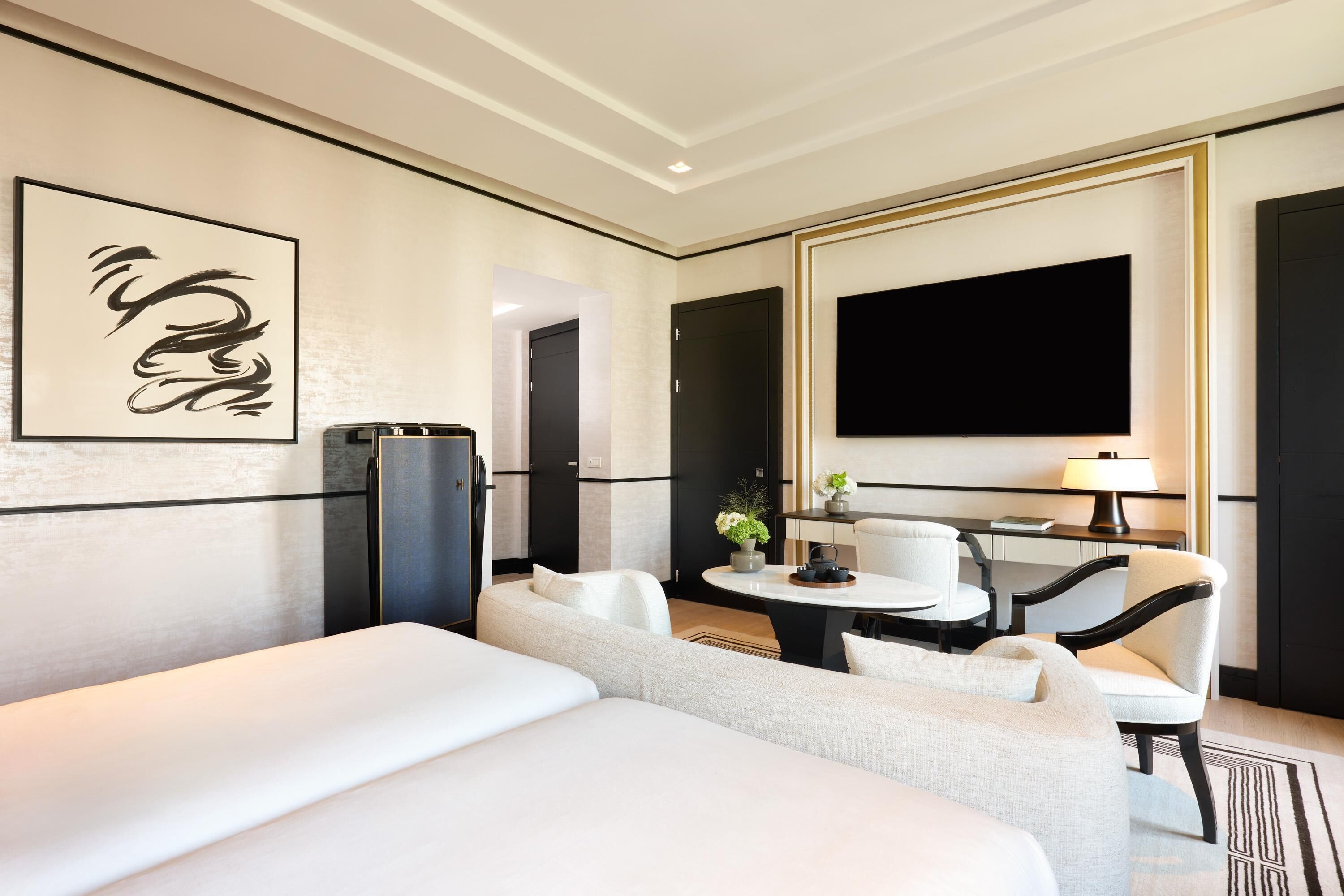 Habitación de hotel con cama, zona de estar con mesa y sillas, televisor de pantalla plana y obras de arte en la pared.