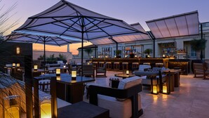 An outdoor bar area with seating and a bar counter, featuring umbrellas and ambient lighting. - Nobu Hotel Roma (Rome)