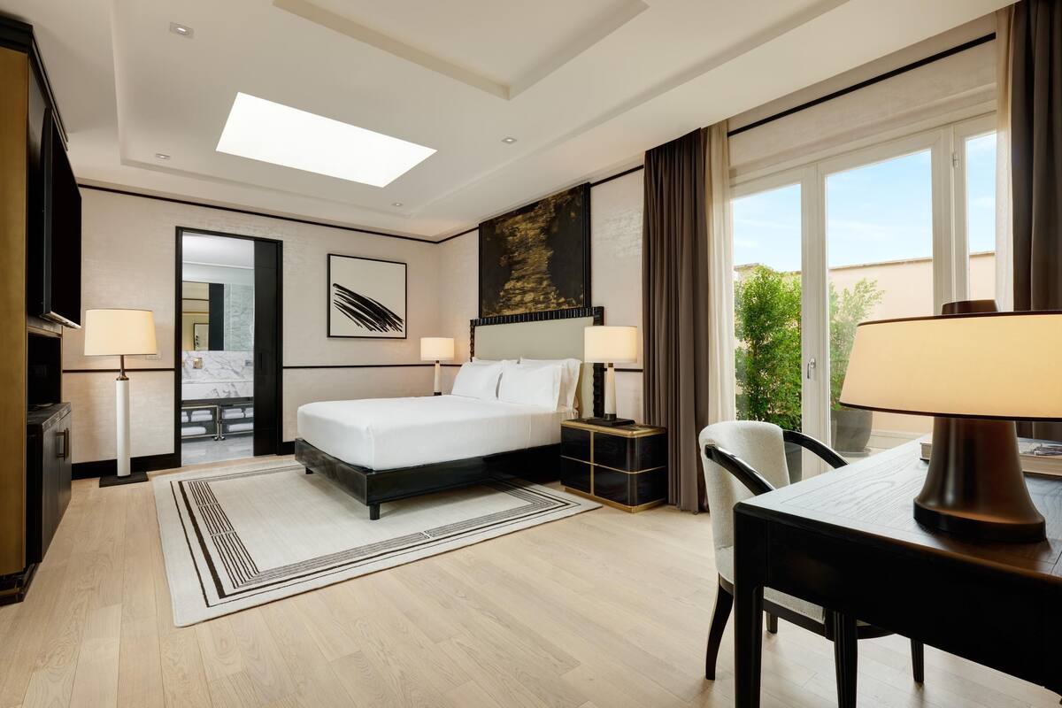 A hotel room with a bed, bedside lamps, a desk, and a chair.