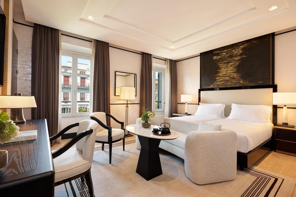 A hotel room with a bed, a desk, a chair, a sofa, and a large window.