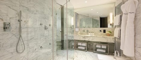 Un baño moderno con ducha de vidrio, paredes de mármol, un espejo grande y tocador con toallas.