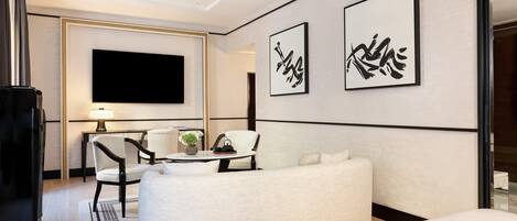Una habitación de hotel moderna con una televisión de pantalla plana, dos obras de caligrafía enmarcadas, un sofá, una mesa de comedor con sillas y una mesita auxiliar.