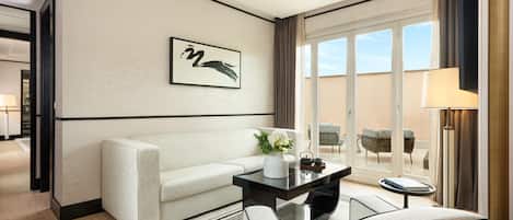 A modern hotel room with a sofa, a coffee table, and a view of the outdoors.