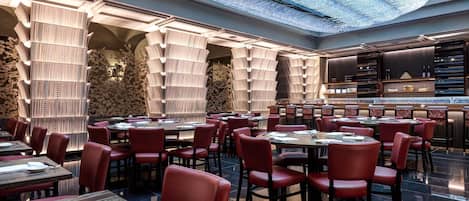 Un restaurante con un interior moderno, con sillas tapizadas en rojo, mesas redondas y un diseño de techo único.