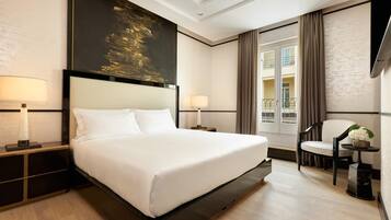 A hotel room with a large bed, two bedside tables with lamps, a chair, a small table with a plant, and a large painting on the wall.