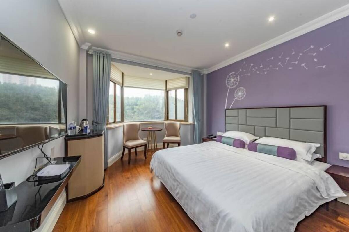 Ein Hotelzimmer mit Bett, Schreibtisch, Stuhl und einem Fenster mit Blick auf Grünflächen.