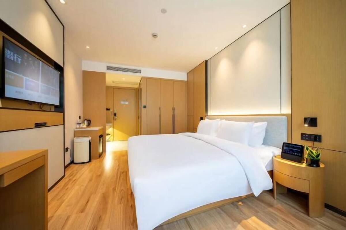 Ein modernes Hotelzimmer mit einem großen Bett, einem Nachttisch mit Radio und einem an der Wand montierten Fernseher.
