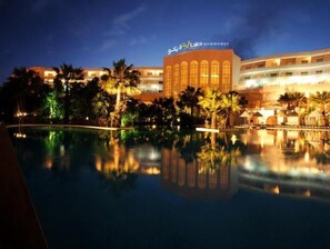 A hotel with a pool reflecting the building and palm trees.