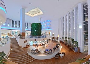 A spacious hotel lobby with a central seating area, multiple floors, and a distinctive green vertical garden. - Laico Hammamet (Hammamet)