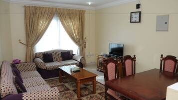 A living room with patterned sofas, a wooden coffee table, a TV, and a dining table with chairs.