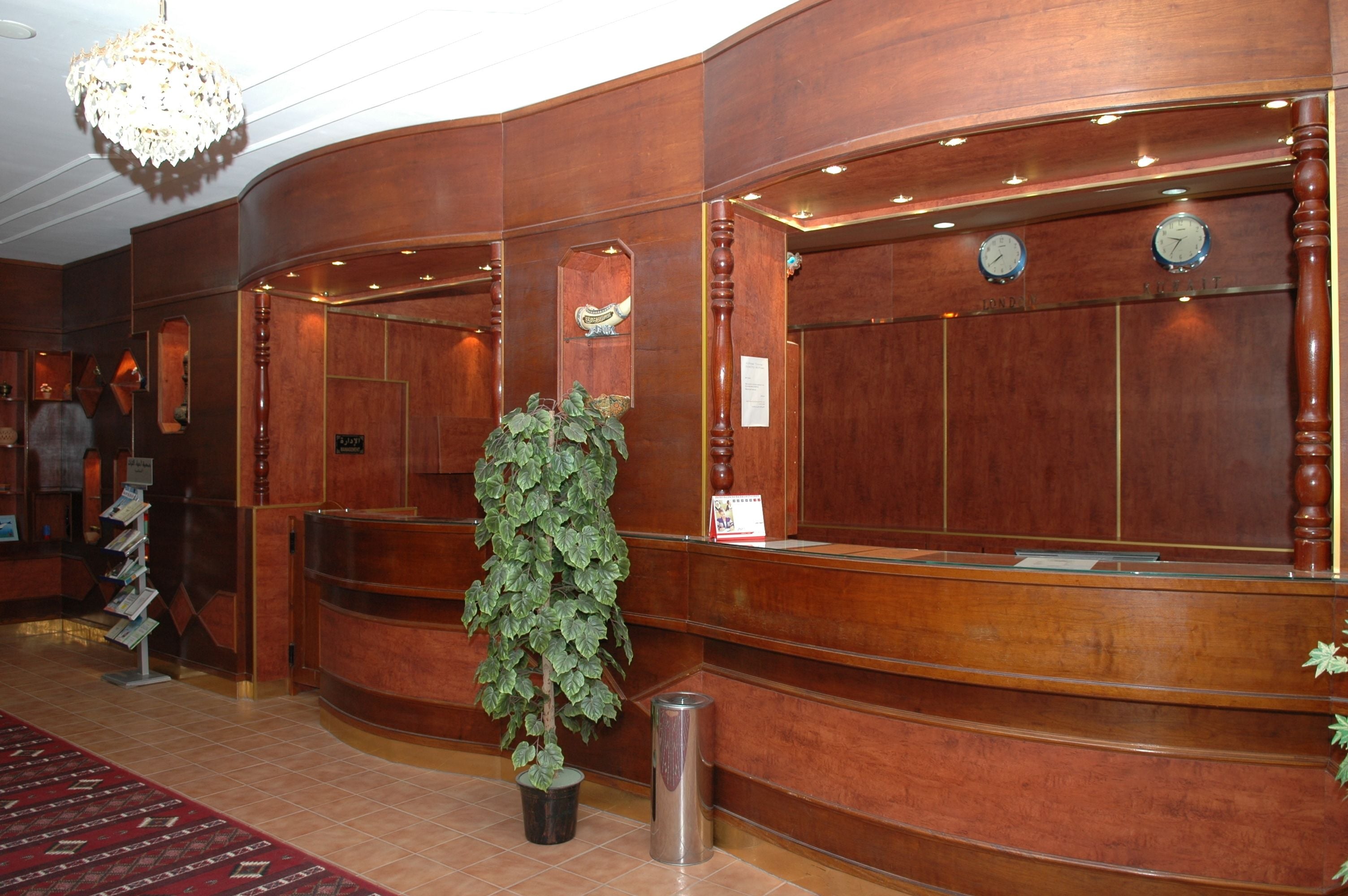 A reception area with a wooden reception desk, a potted plant, a trash can, and a chandelier.