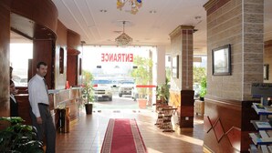 Un hall de hotel con una recepción, una alfombra roja y vistas a coches aparcados fuera.