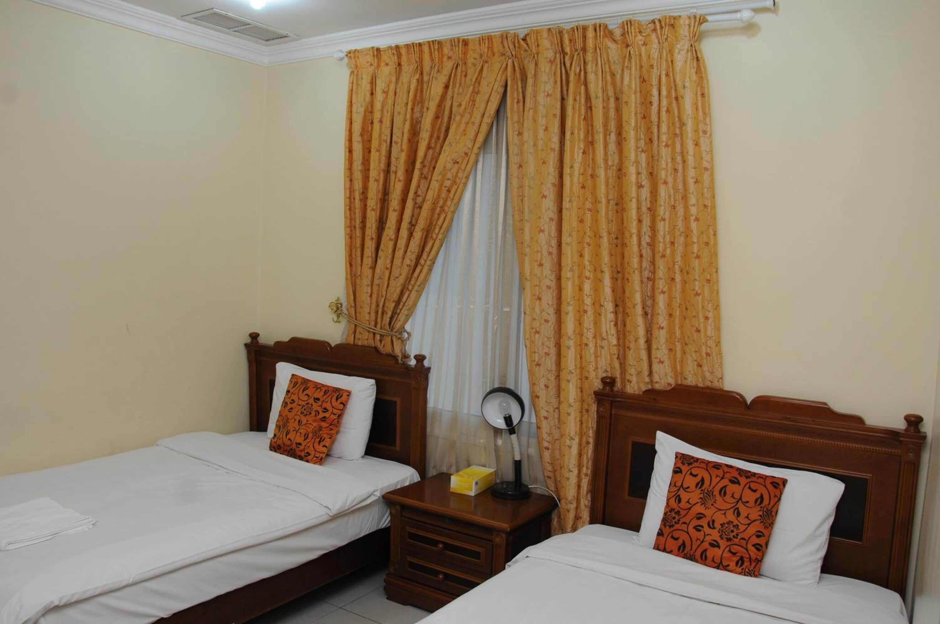 A hotel room with two single beds, wooden headboards, and a nightstand with a lamp.