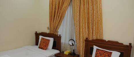 A hotel room with two single beds, wooden headboards, and a nightstand with a lamp.
