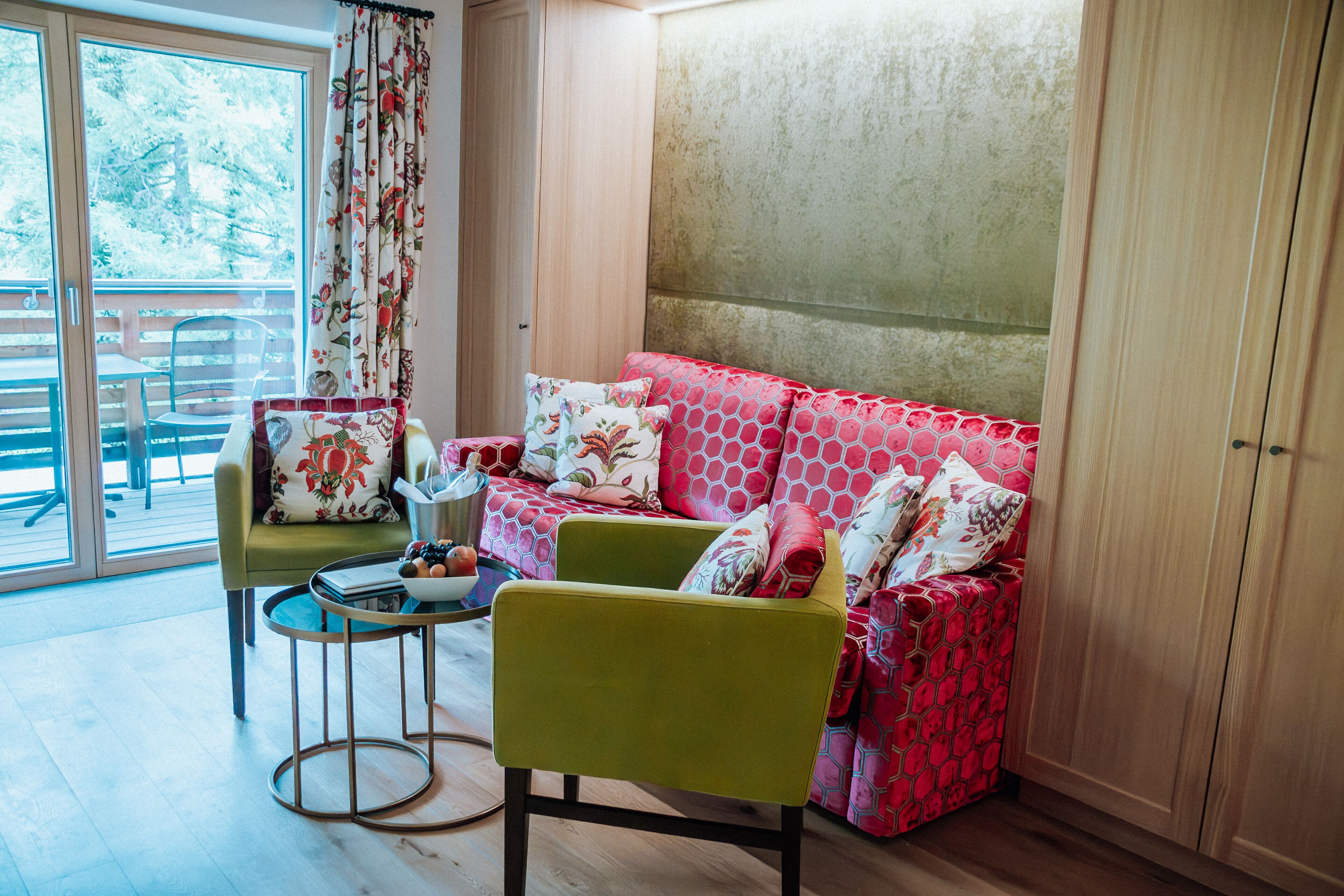 A room with a green sofa, a red patterned sofa, a small table with a bowl of fruit, and a chair.