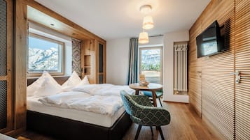 A bedroom with a bed, a chair, a table, a TV, and a window with a mountain view.
