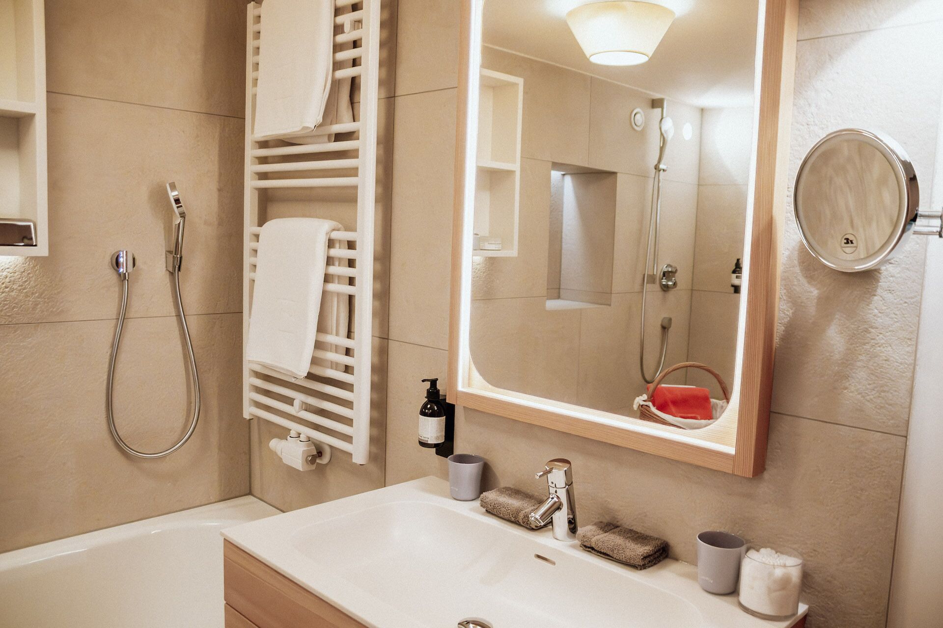 A modern bathroom with a bathtub, a sink, a mirror, a towel rack, and a shower.