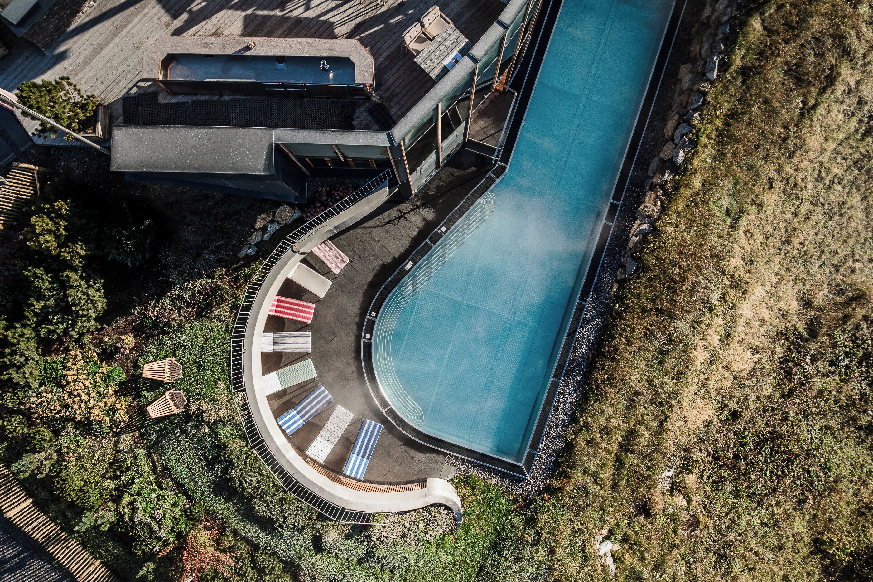 Vue aérienne d’une piscine dotée d’une terrasse incurvée, entourée de verdure et bordée d’un bâtiment à toit plat.