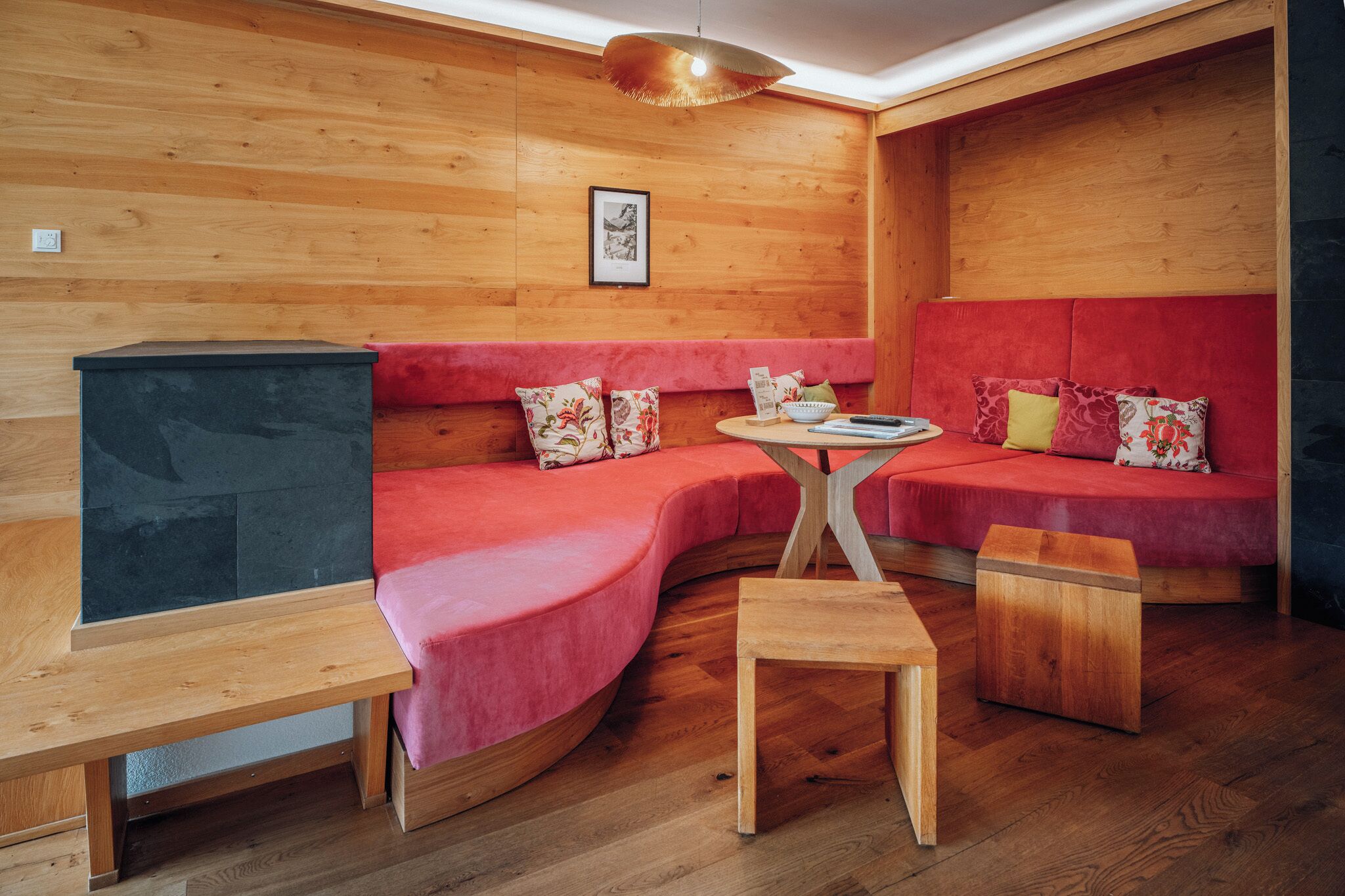 Ein gemütliches Zimmer mit Holzwänden, einem bogenförmigen roten Sofa, einem kleinen Holztisch und einer Bank.