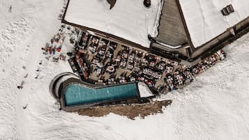 Une vue aérienne d’un hôtel avec une piscine, entouré d’un paysage enneigé et d’un parking.