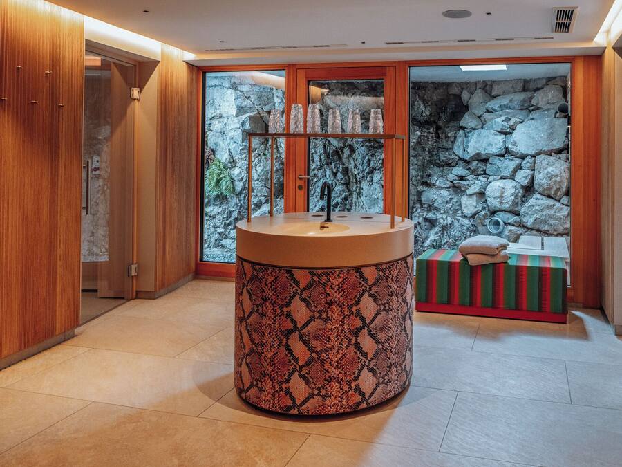 A bathroom with a circular sink, wooden cabinets, and a stone wall backdrop.