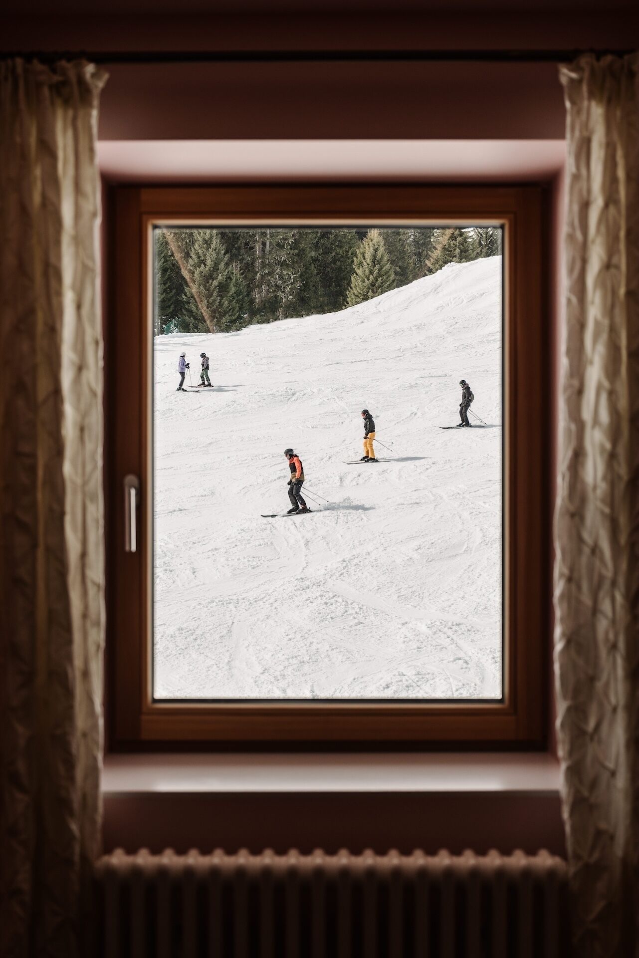 Una ventana con vistas a una ladera nevada, enmarcada por cortinas.