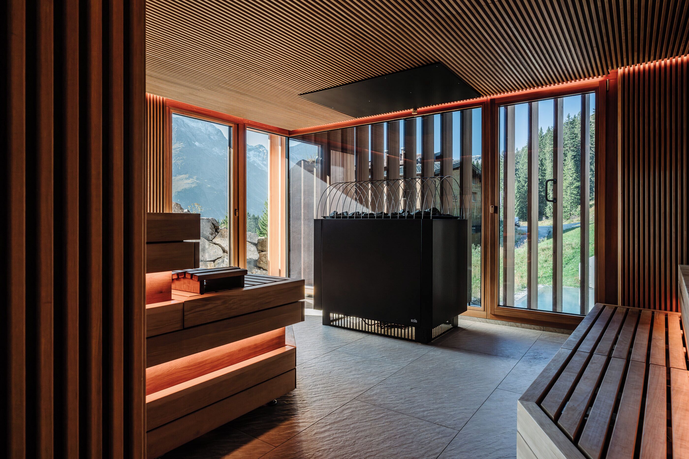 A modern interior with a wooden bench, a black cabinet, and large windows offering a mountain view.