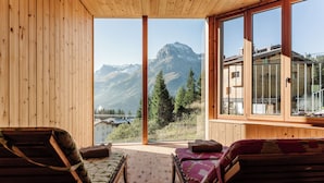Un interior de madera con dos sofás orientados hacia una ventana grande con vistas a las montañas.