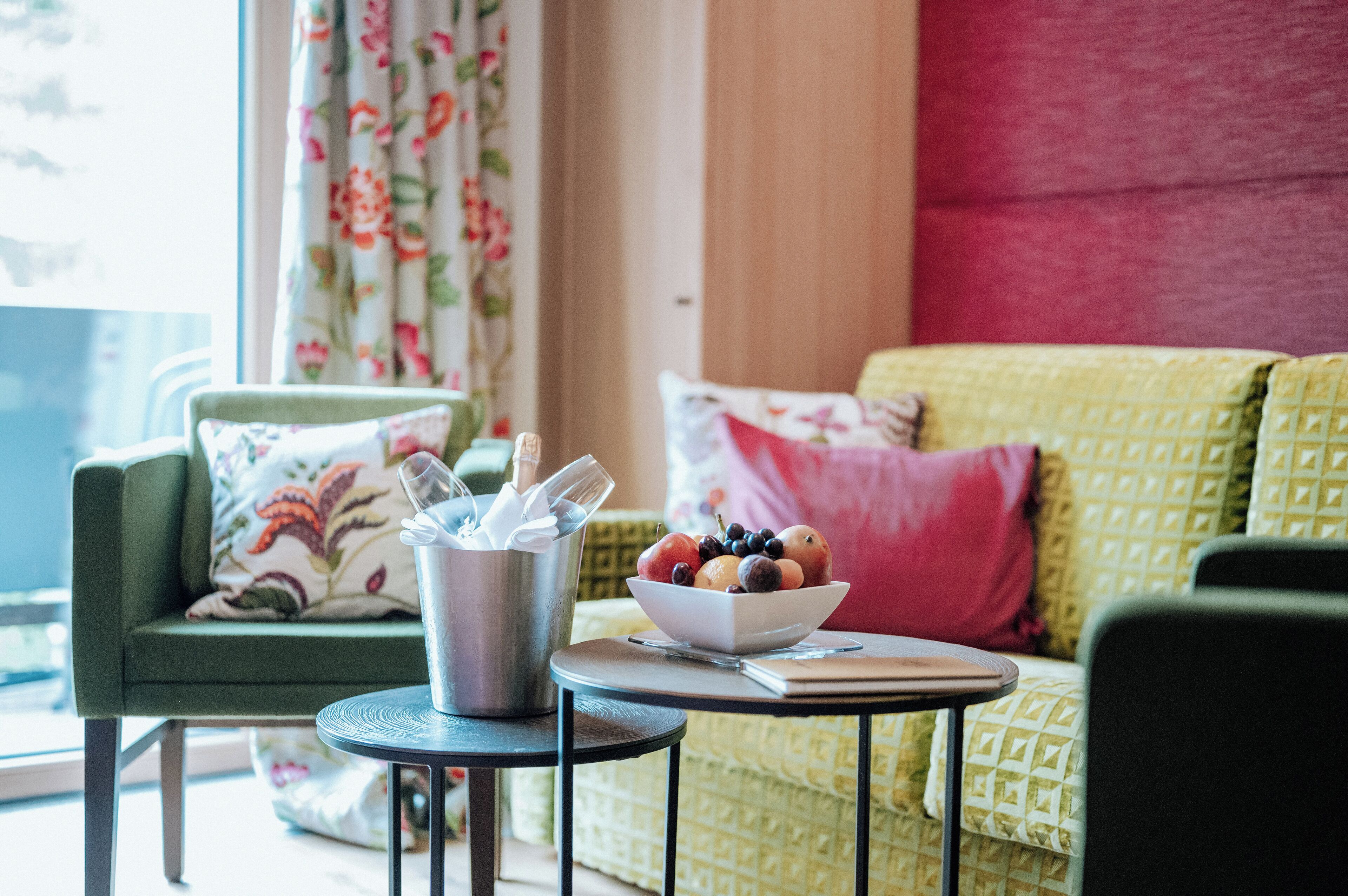 A cozy living room with a green sofa, a small round table with a bowl of fruit, and a metal container with utensils.