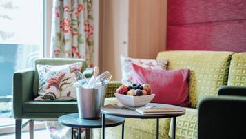 A cozy living room with a green sofa, a small round table with a bowl of fruit, and a metal container with utensils.
