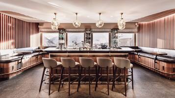 Uma área de bar moderna com detalhes em madeira, banquetas e iluminação pendente.