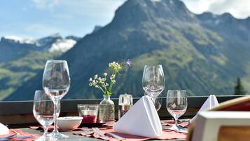 Una mesa servida con copas de vino, un florero con flores y condimentos, con vistas a una cadena montañosa.