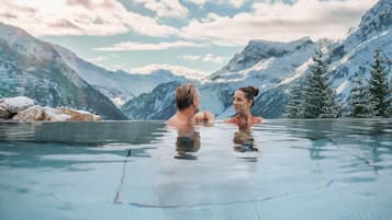 Un couple se trouve dans une piscine aux eaux cristallines, avec un paysage montagneux en arrière-plan.