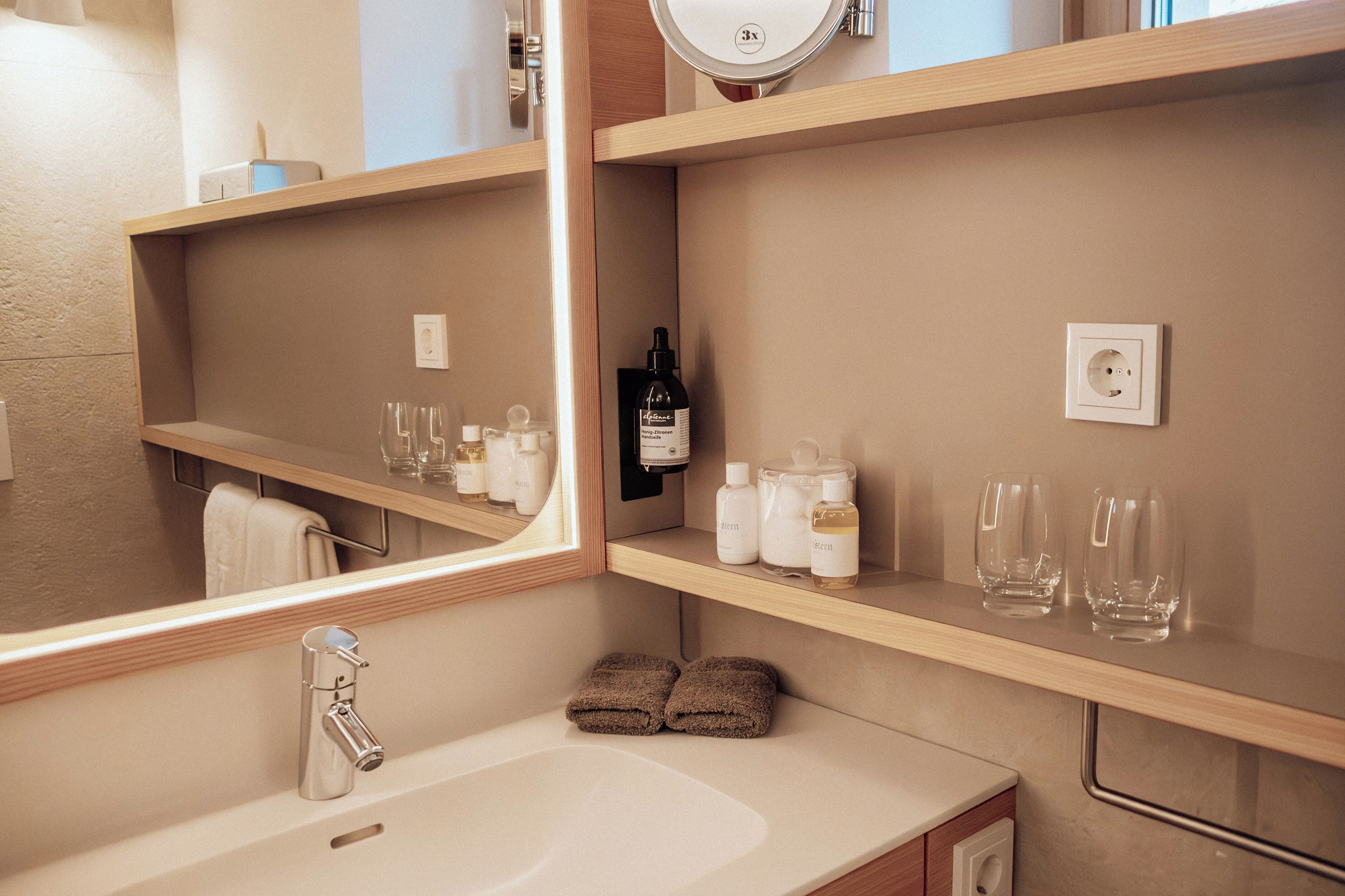 Un baño moderno con un espejo grande, un lavabo y repisas con artículos de tocador.