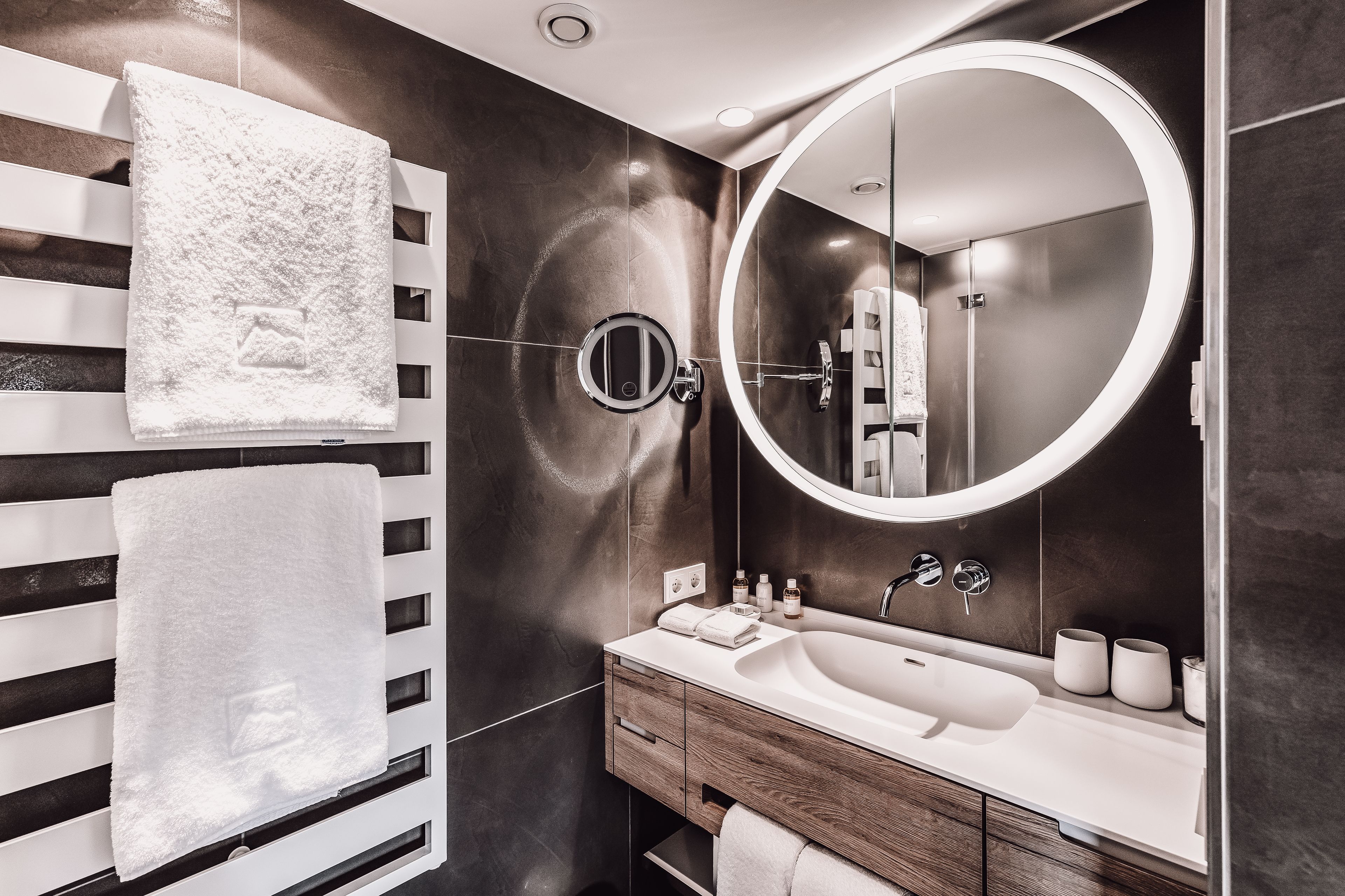 Un baño moderno con un espejo grande, lavamanos blanco y perchero para toallas.