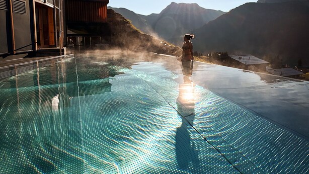 Una piscina infinita con vistas despejadas a montañas al fondo.