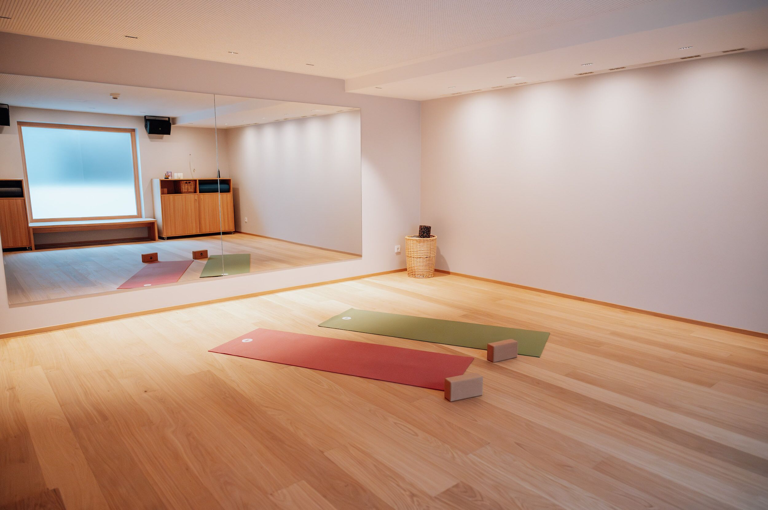 Ein geräumiger Raum mit einem großen Spiegel, Holzboden und einer Yogamatte.